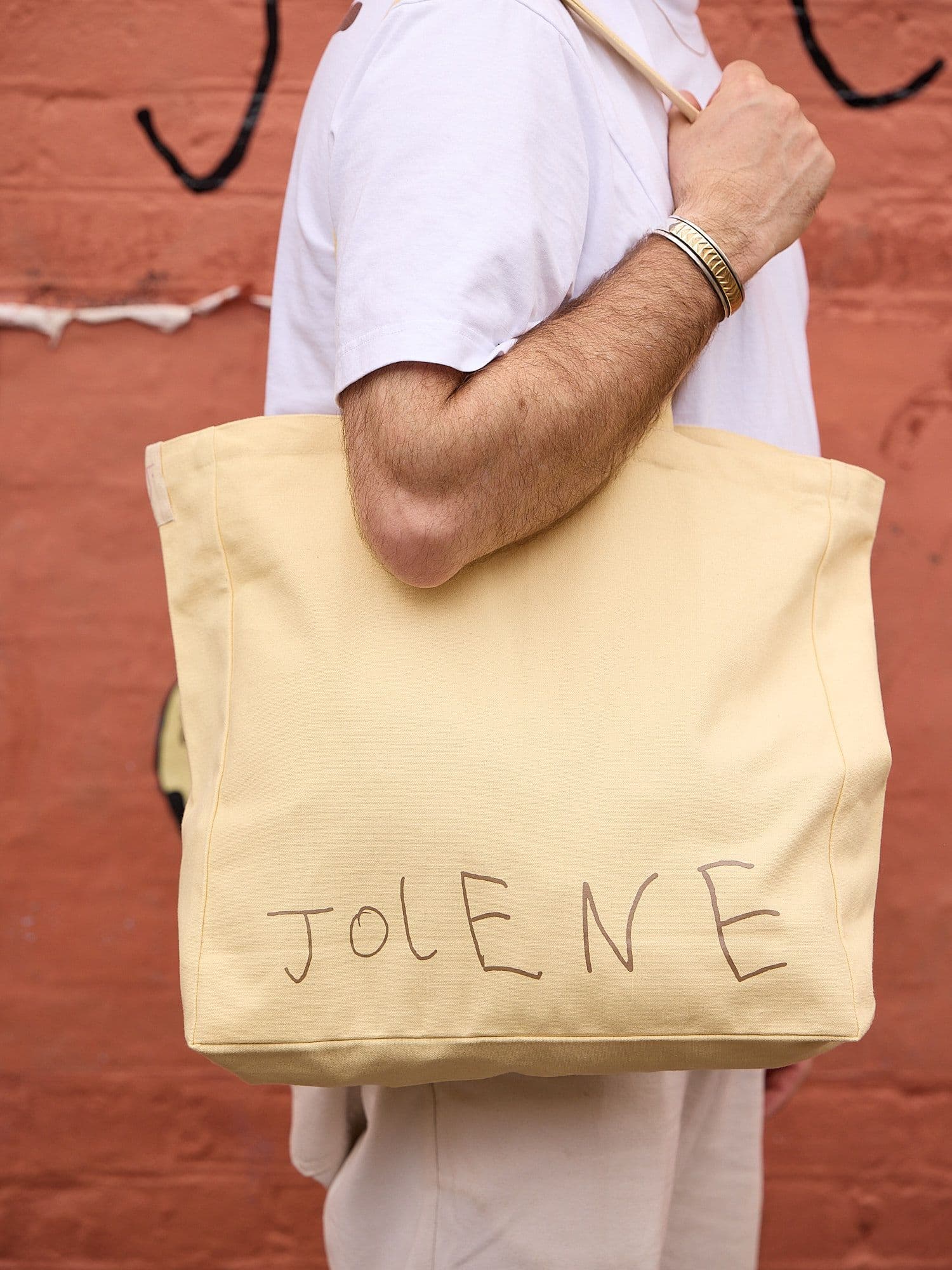 The Jolene Small Tote in stone pictured on a man's shoulder standing outside Jolene Redchurch Street