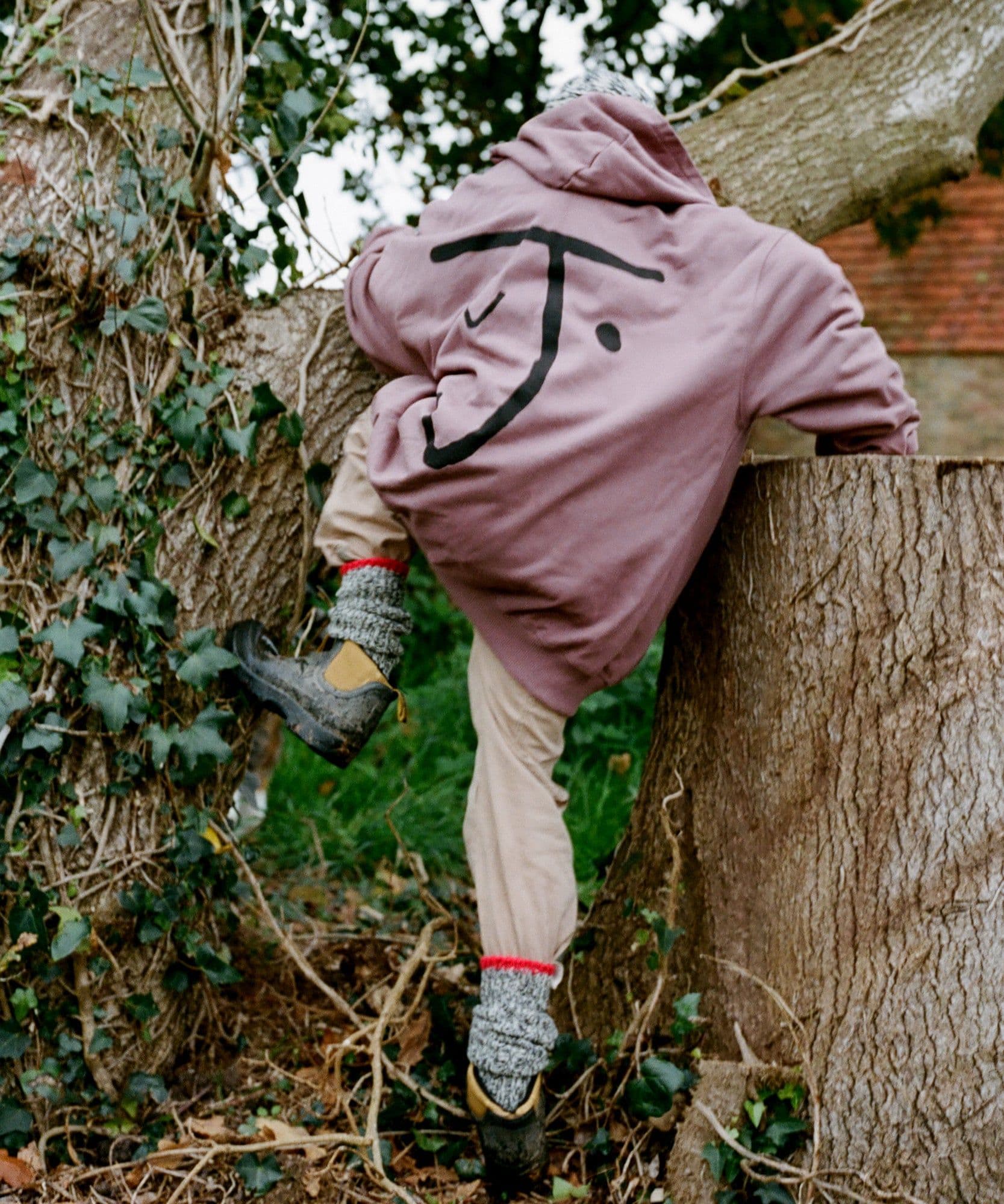 A model wearing the Jolene bakery J face hoodie while climbing a tree