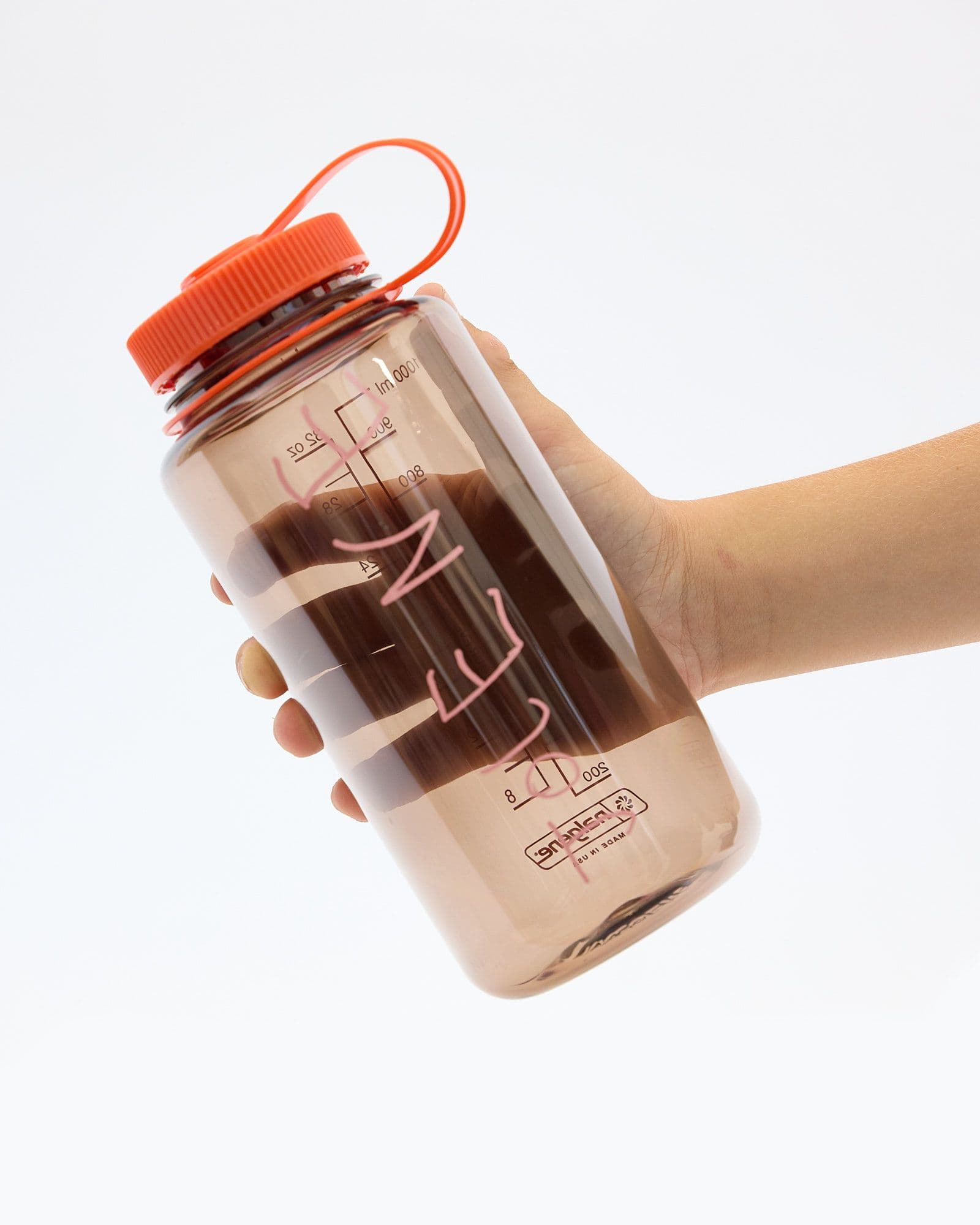 A studio product shot of the Jolene bakery x Nalgene Refill Water Bottle. The bottle is brown with a pink Jolene logo and bright orange top