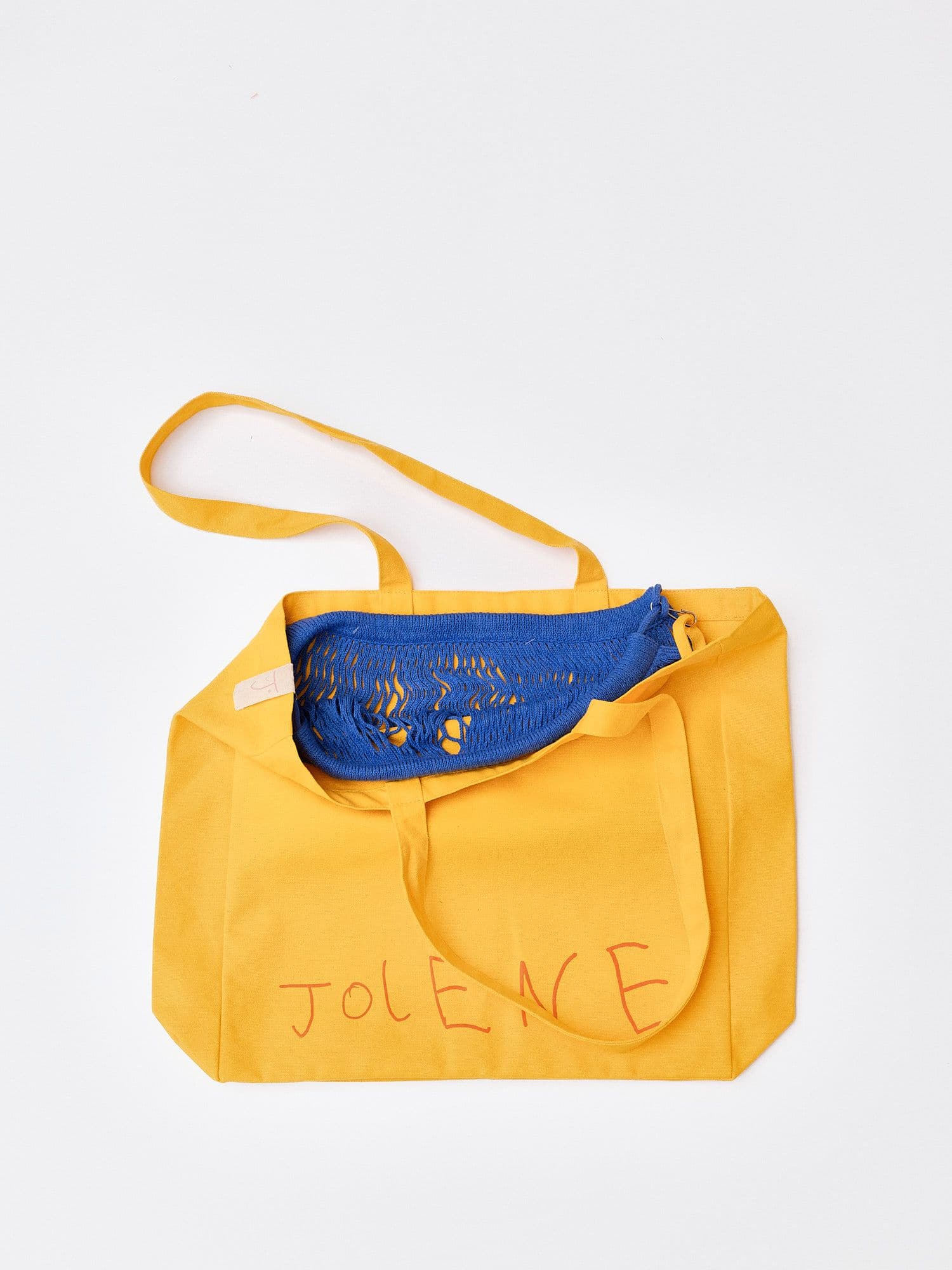 The Jolene bakery yellow tote bag with the blue net pocket inside it pictured on a white background