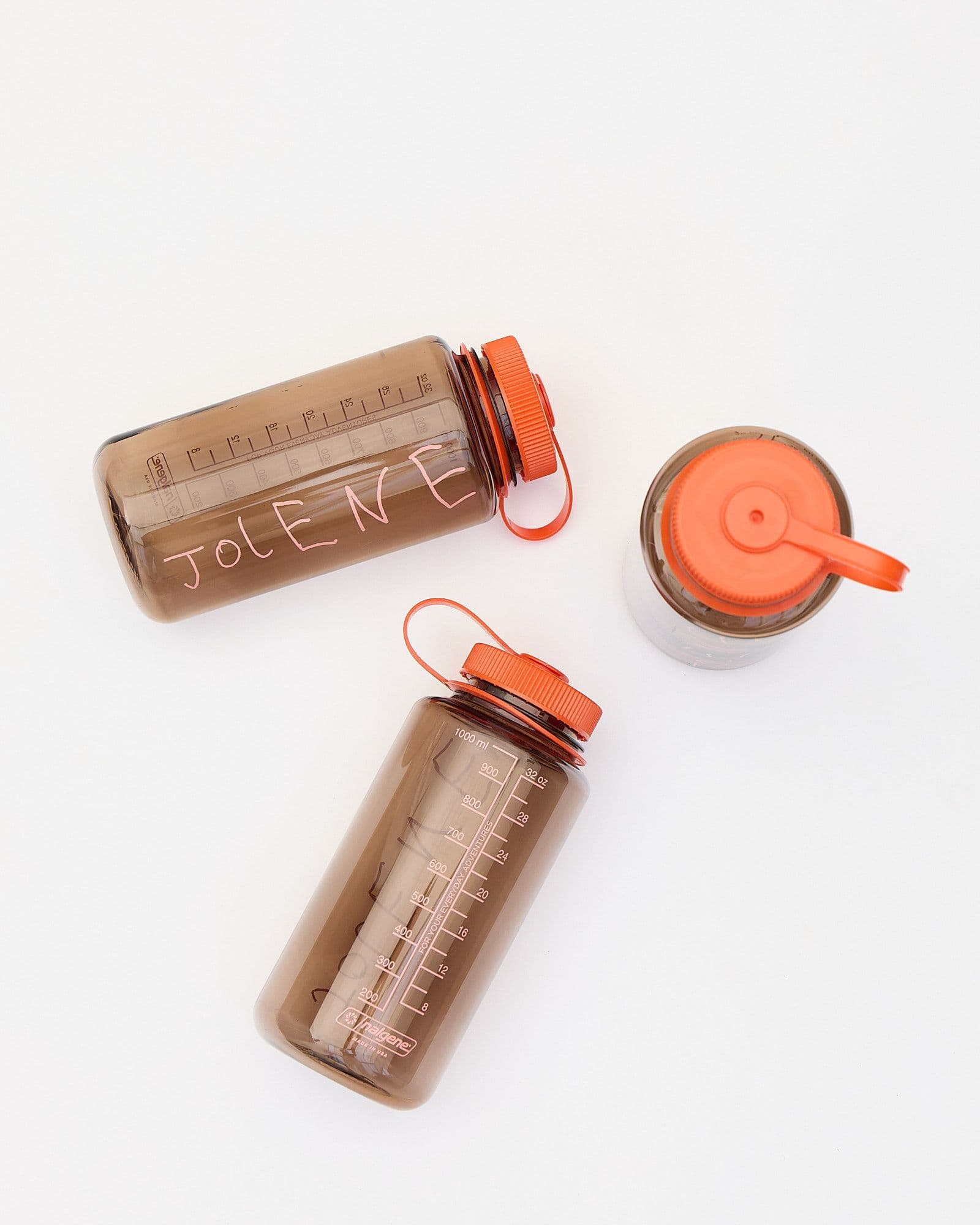 A studio product shot of the Jolene bakery x Nalgene Refill Water Bottle. The bottle is brown with a pink Jolene logo and bright orange top