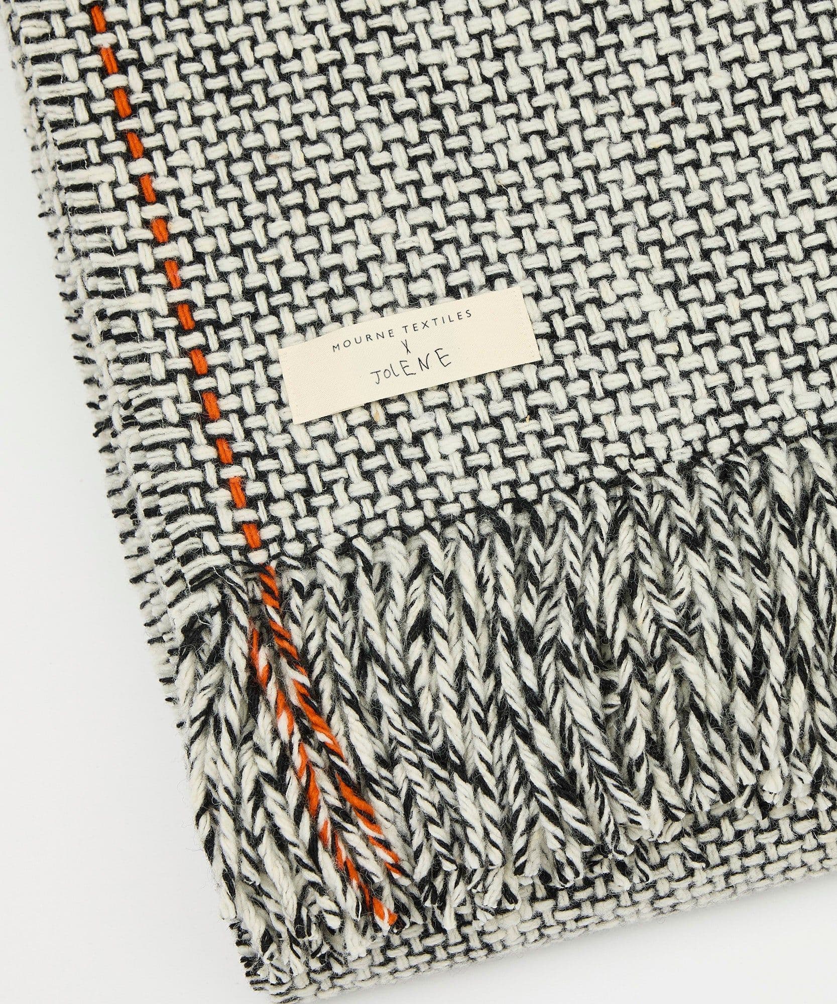 A product image of the Jolene x Mourne Textiles blanket on a white background. It shows the black and white blanket folded up showing the label and detail of the weave