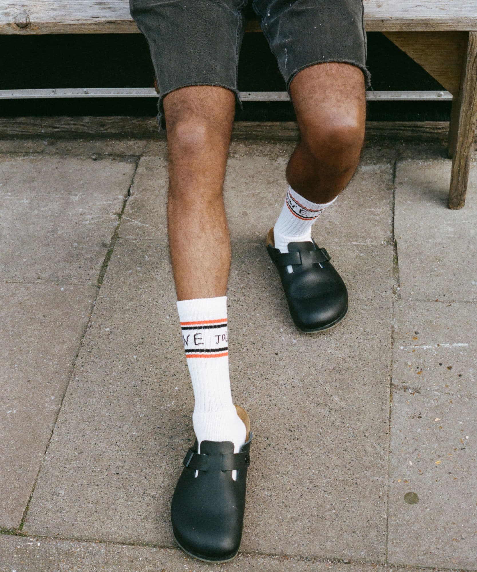 A male model sitting outside wearing the Jolene J socks and some leather birkenstocks