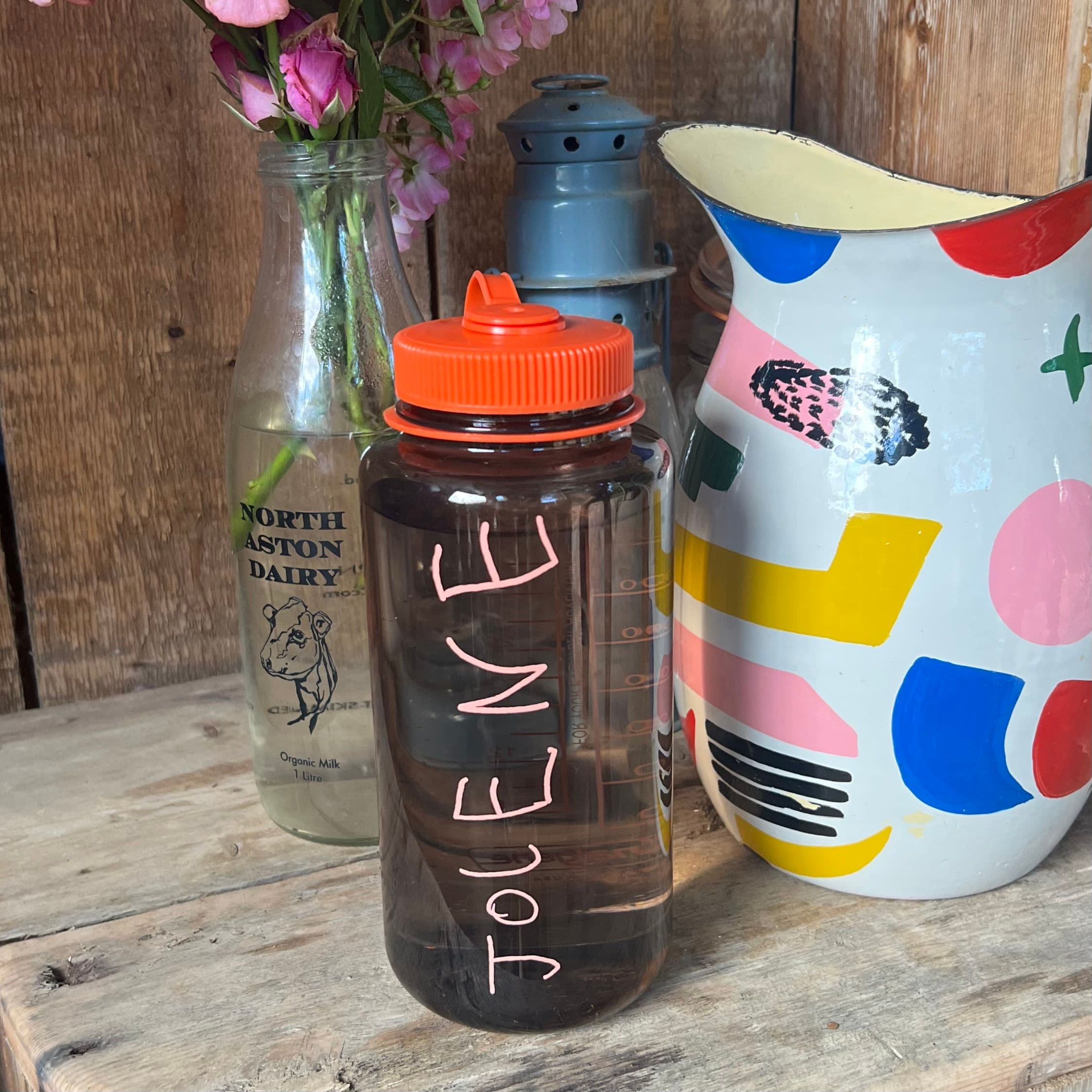 The Jolene refillable water bottle pictured on a wooden worktop with a colourful jug at the Whichford Mill sauna