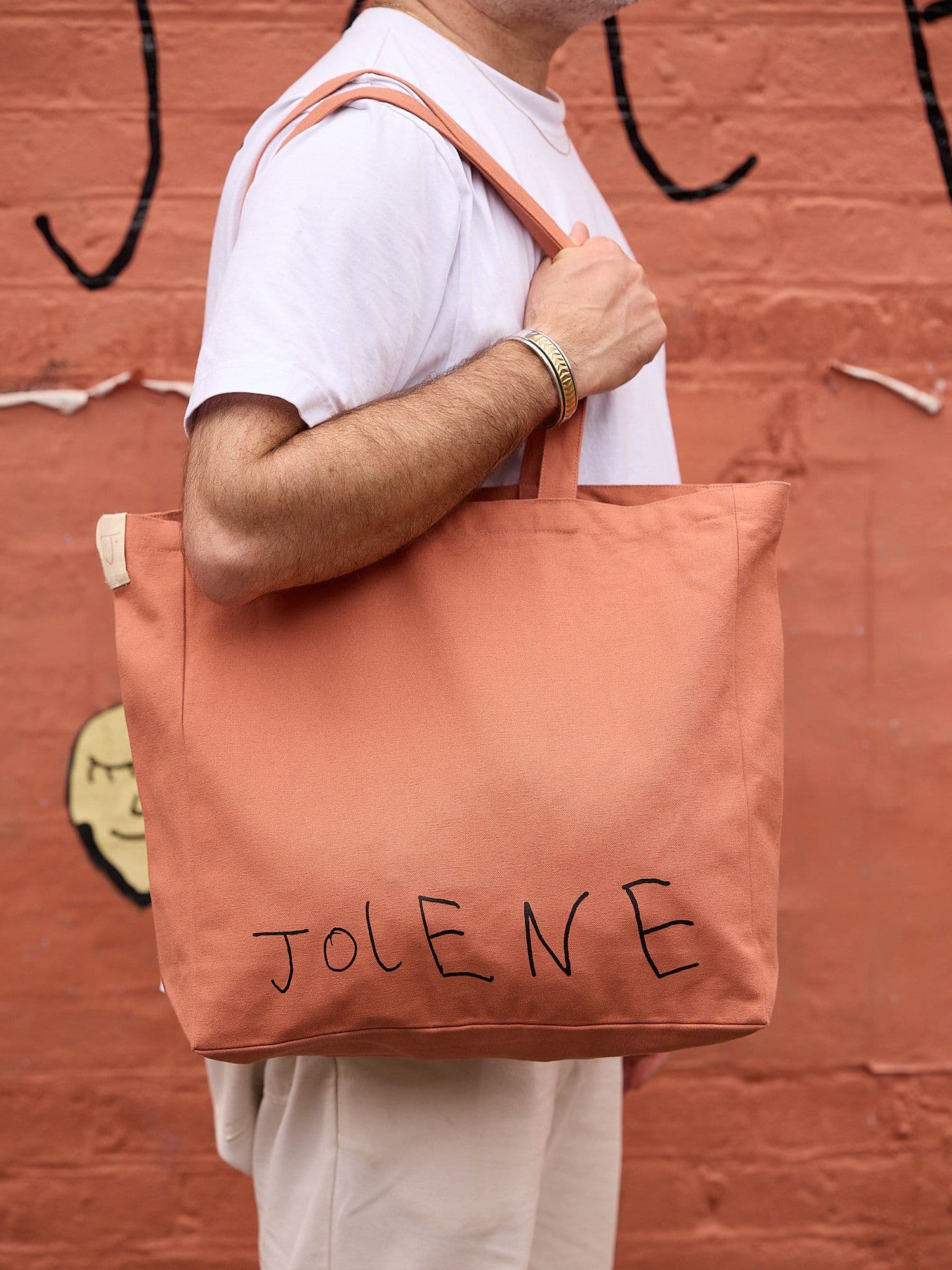 The Jolene Small Tote in pink pictured on a man's shoulder standing outside Jolene Redchurch Street