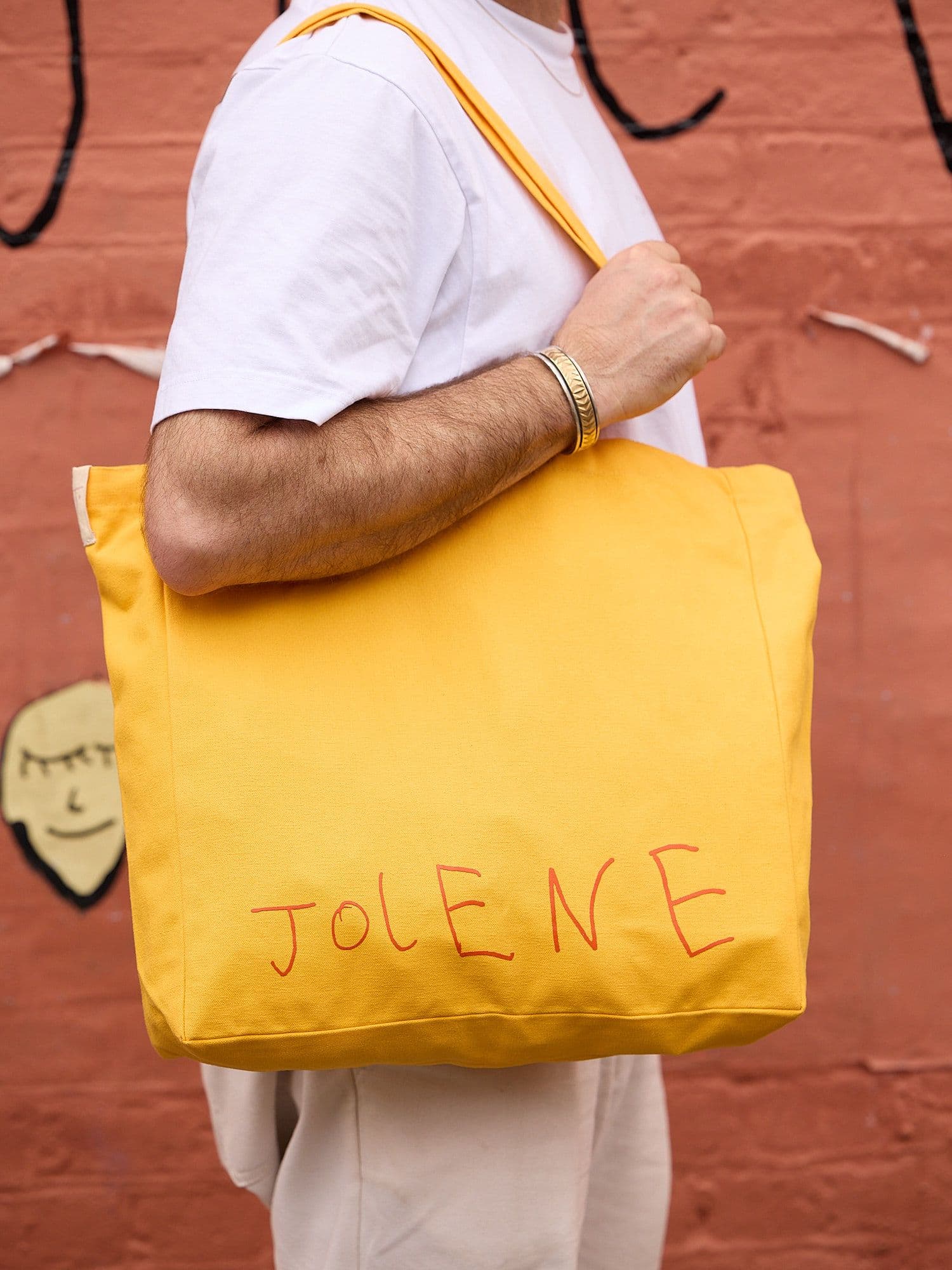 The Jolene Small Tote in yellow pictured on a man's shoulder standing outside Jolene Redchurch Street