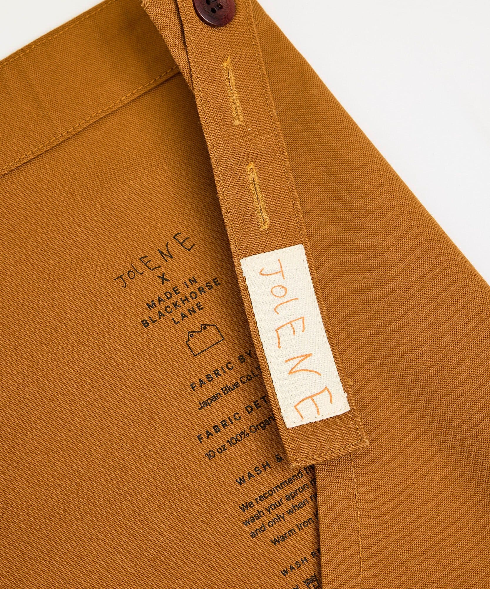 The label and branding of the Jolene Bakery house apron in caramel colour